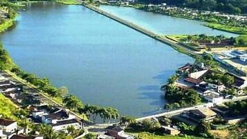 Vista aérea de uma área residencial com casas ao longo de um rio, uma ponte e um edifício grande ao fundo.