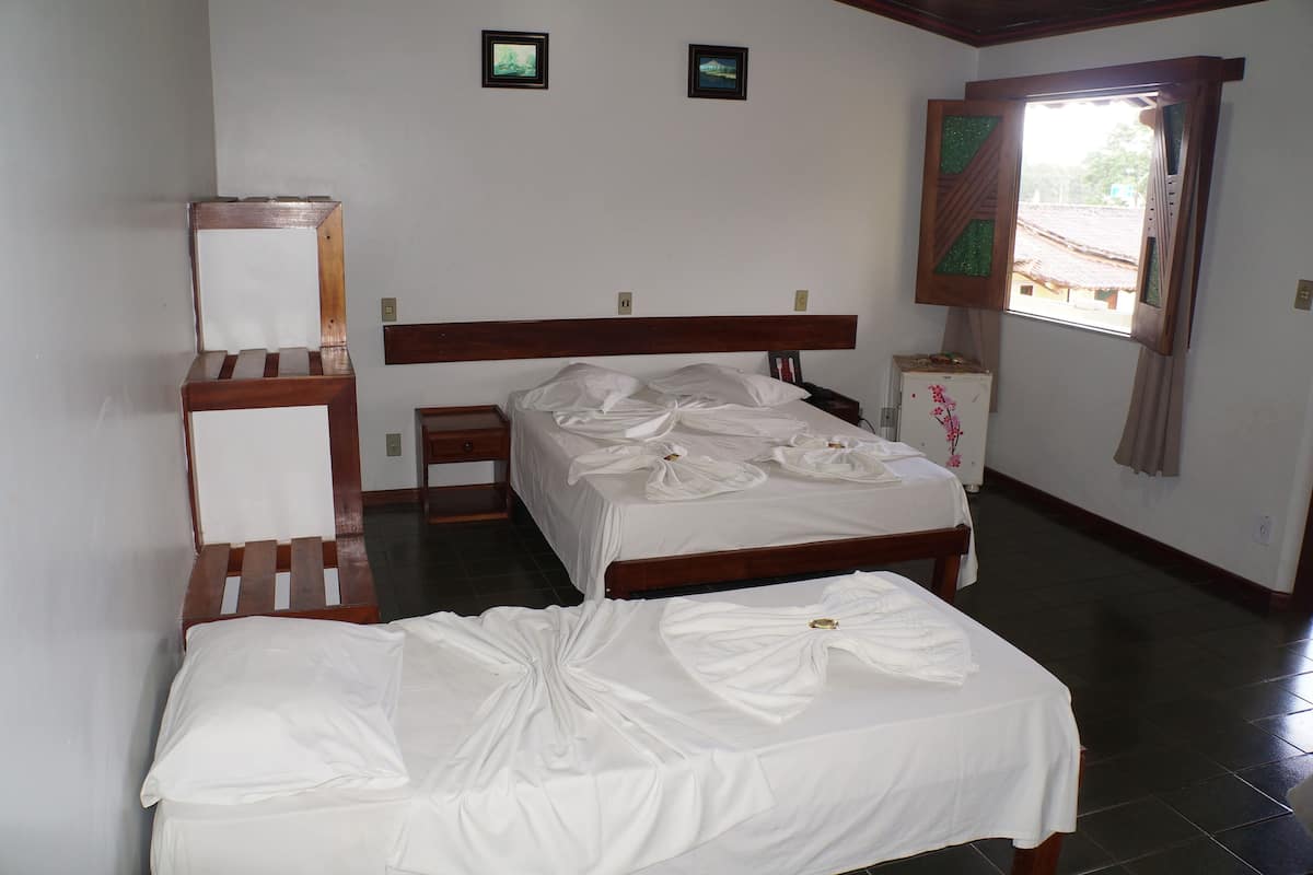 A bedroom with a wooden bed, a wooden nightstand, a mirror, and a window with curtains.