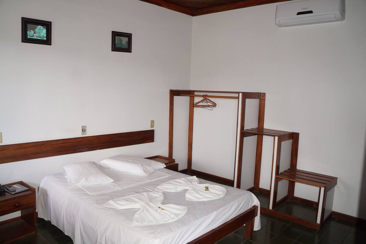 A neatly made bed with white linens, a wooden headboard, and a wooden bedside table with a lamp.