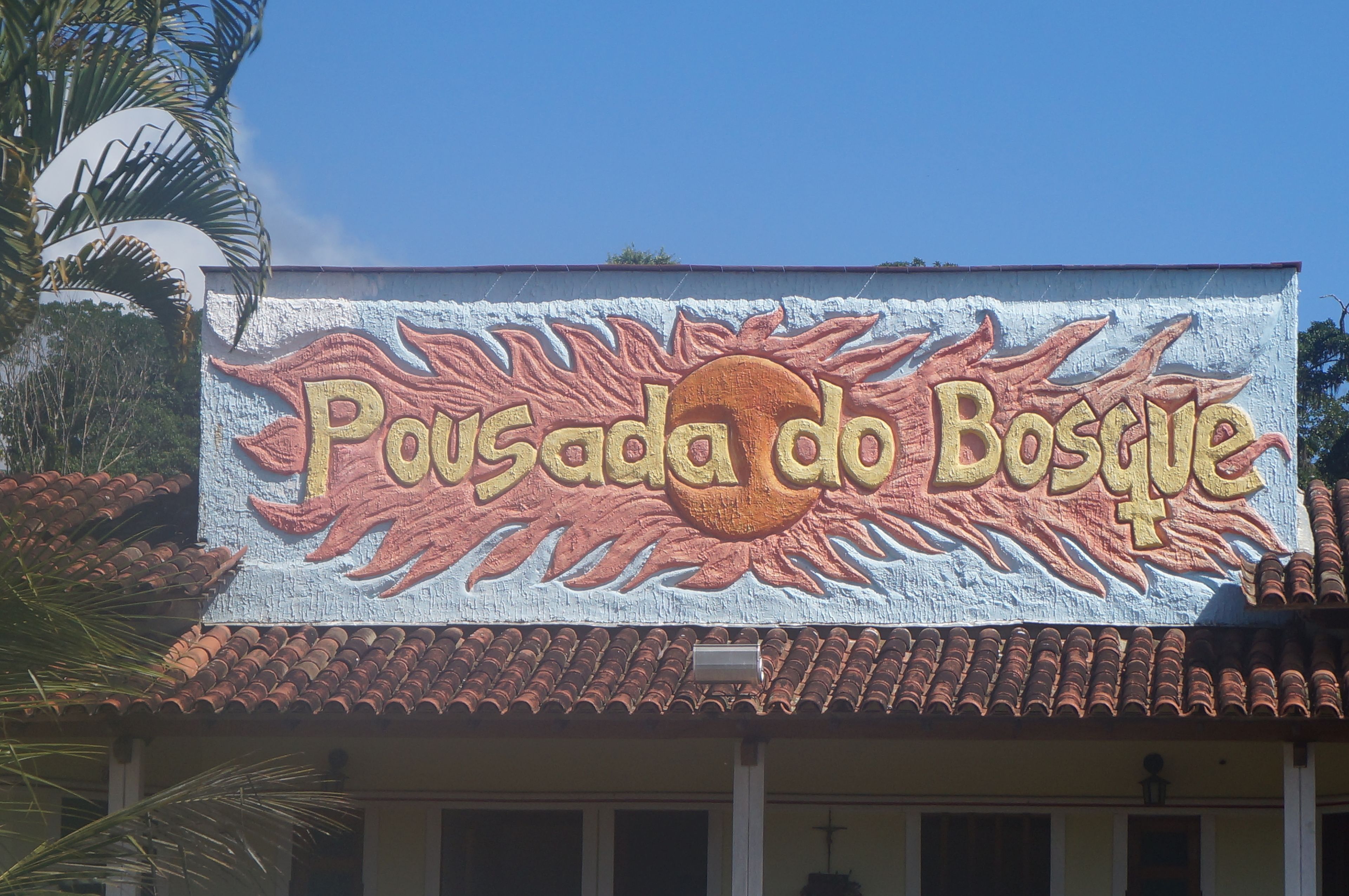 A building with a mural of a sun and the text "Pousada do Bosco".