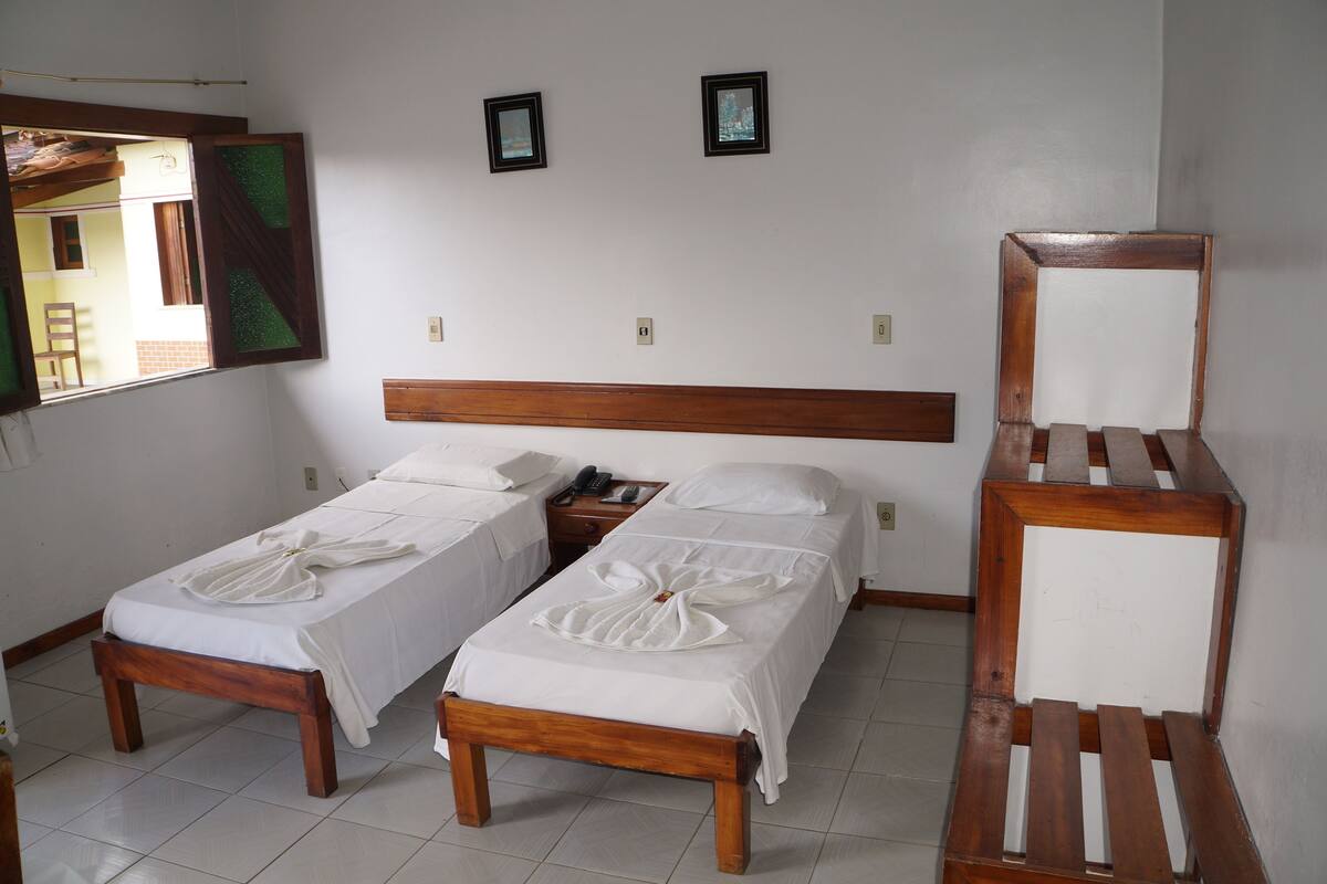 A hotel room with two single beds, a wooden headboard, a small bedside table with a phone, and a mirror.