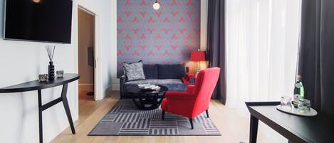 Un salon moderne avec un canapé, un fauteuil rouge, une table basse et un téléviseur fixé au mur.
