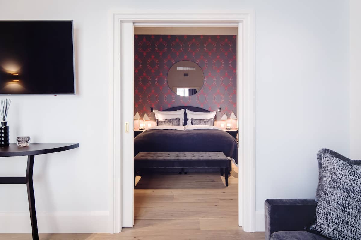 A bedroom with a bed, bedside lamps, a round mirror, and a TV on the wall.