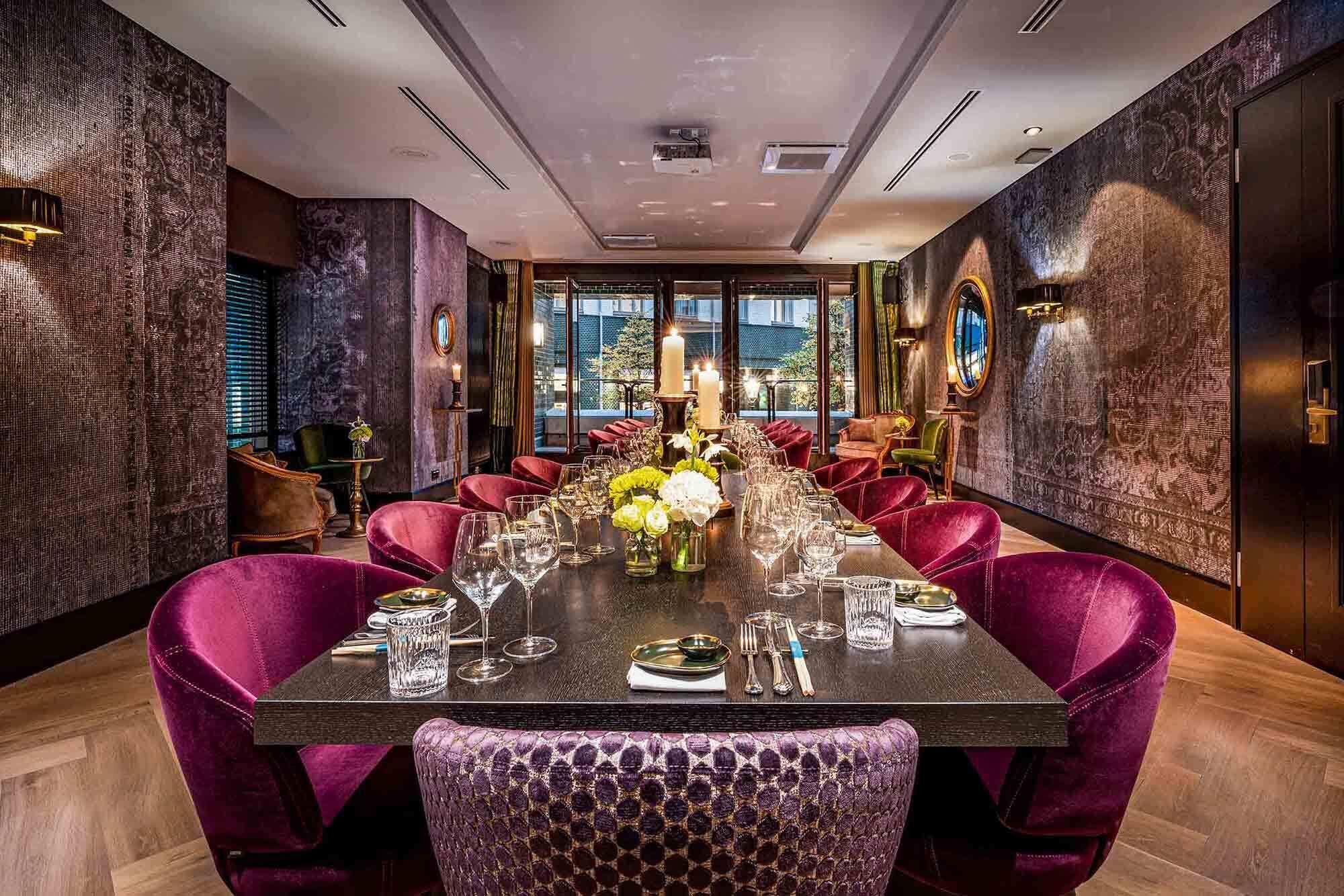 A long dining table set with chairs, candles, and a view of the city through large windows.