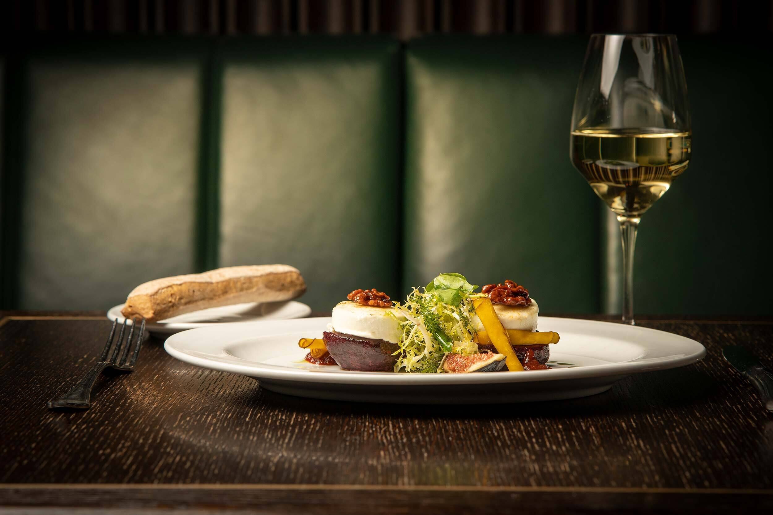 Un plato de comida con una copa de vino blanco sobre una mesa de madera.