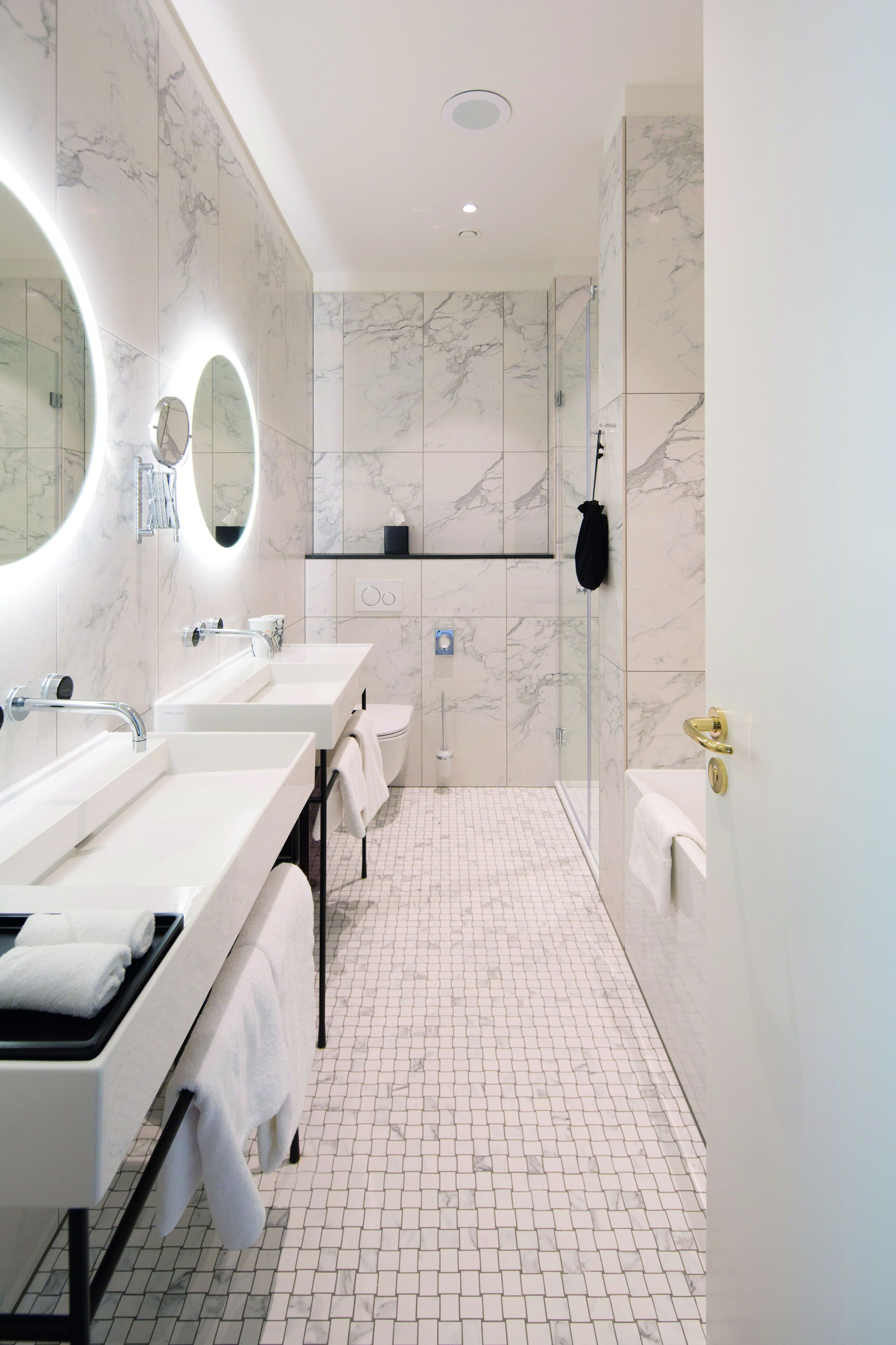 A modern bathroom with marble walls, two sinks, a glass shower enclosure, and a towel rack.