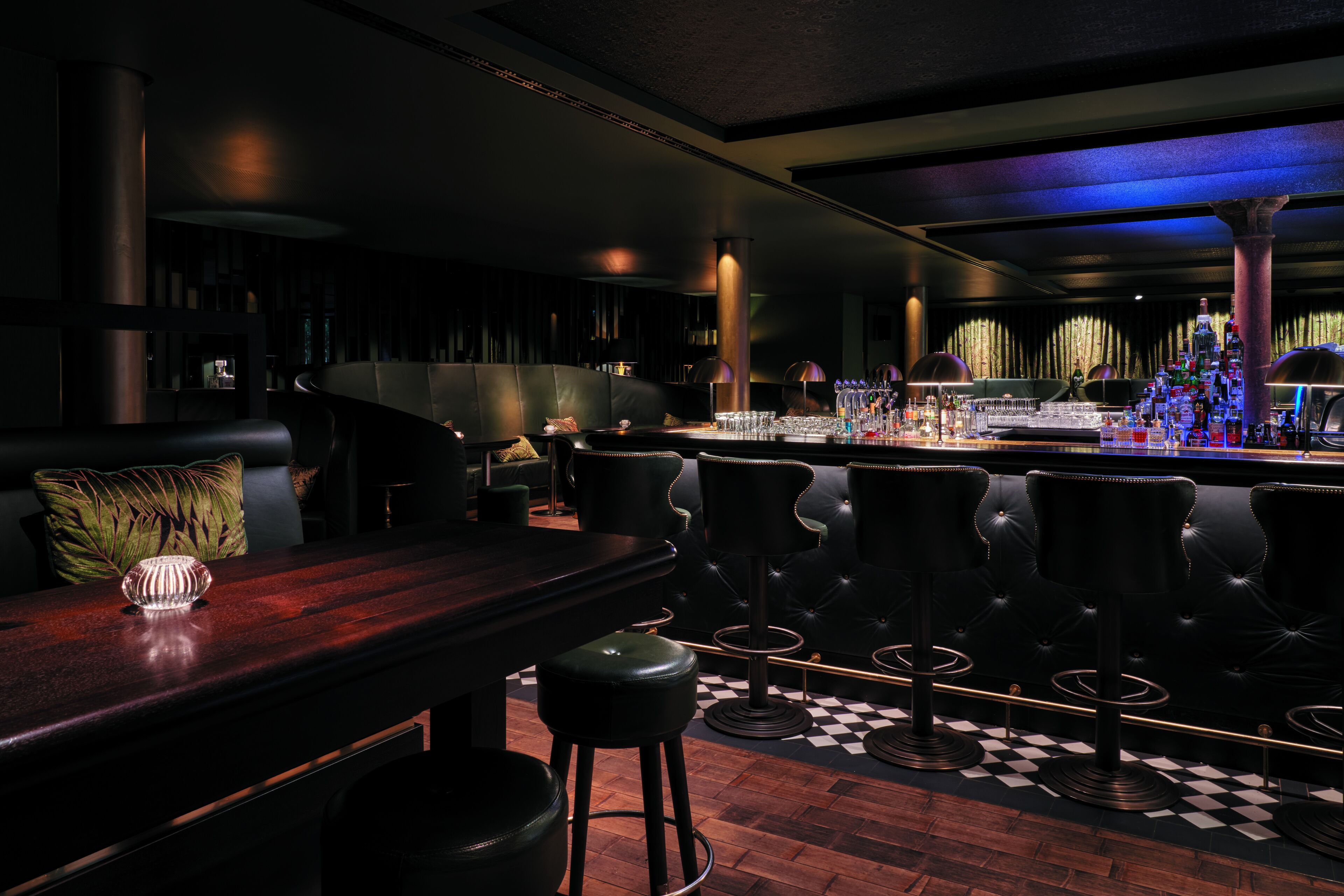 A bar area with a checkered floor, black leather bar stools, and a bar counter with a bottle of liquor.