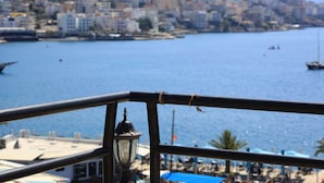A coastal cityscape with buildings along the waterfront, a clear blue sea, and a view through a metal railing. - Hotel Real (Sarandë)