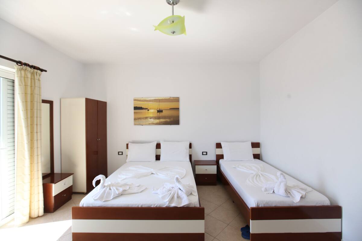 A hotel room with two beds, a wardrobe, a painting, and a window with curtains.