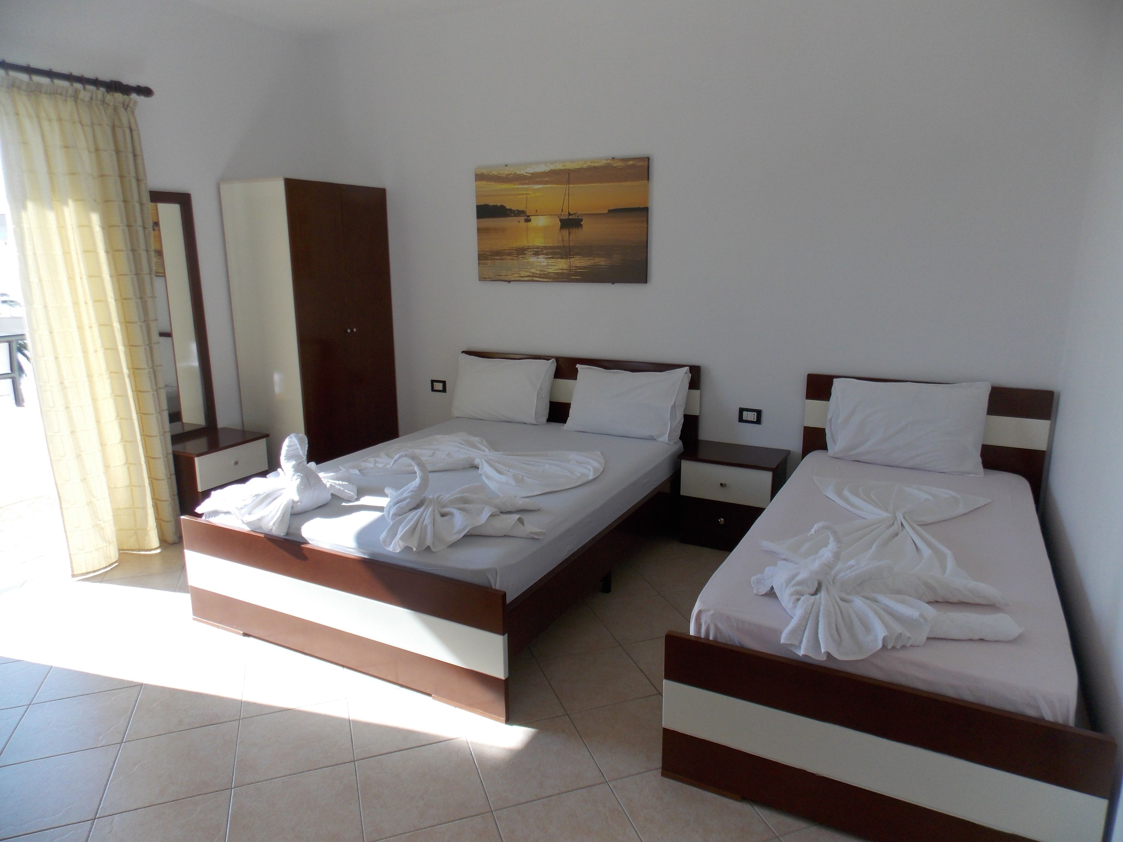 A hotel room with two beds, a painting on the wall, and a mirror.
