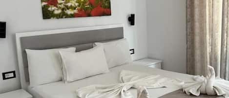 Una cama bien hecha con sábanas blancas y un arreglo decorativo de almohadas con forma de cisne, un cabecero gris y un cuadro de flores en la pared.