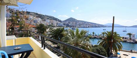 A balcony with a view of a marina, palm trees, and a cityscape in the background.