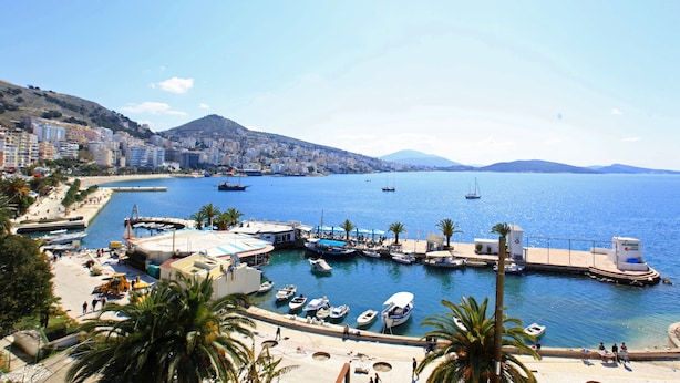 A coastal marina with boats docked, a pier, and a mountainous backdrop. - Hotel Real (Sarandë)