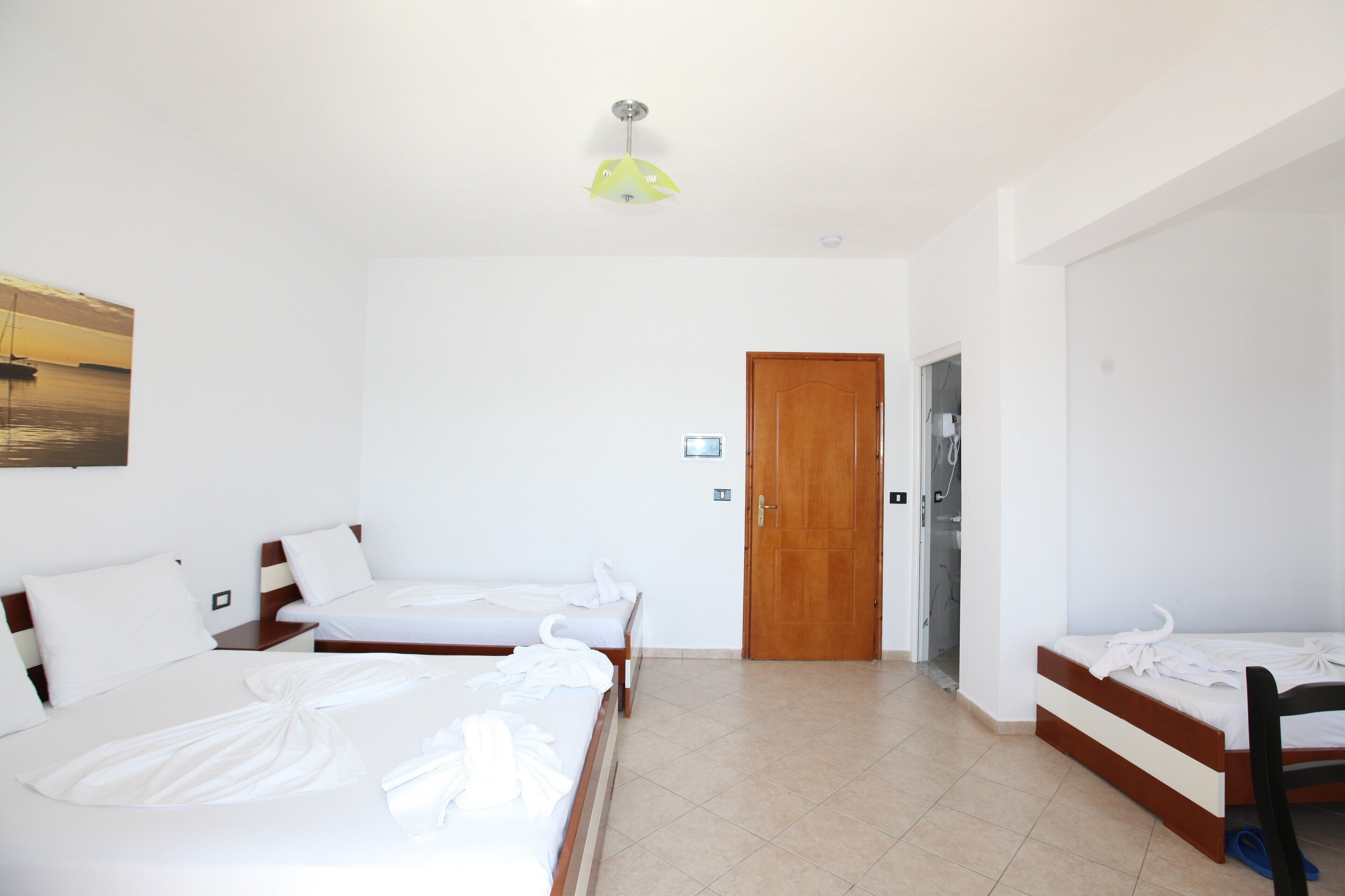 A hotel room with three beds, a wooden door, and a ceiling light.