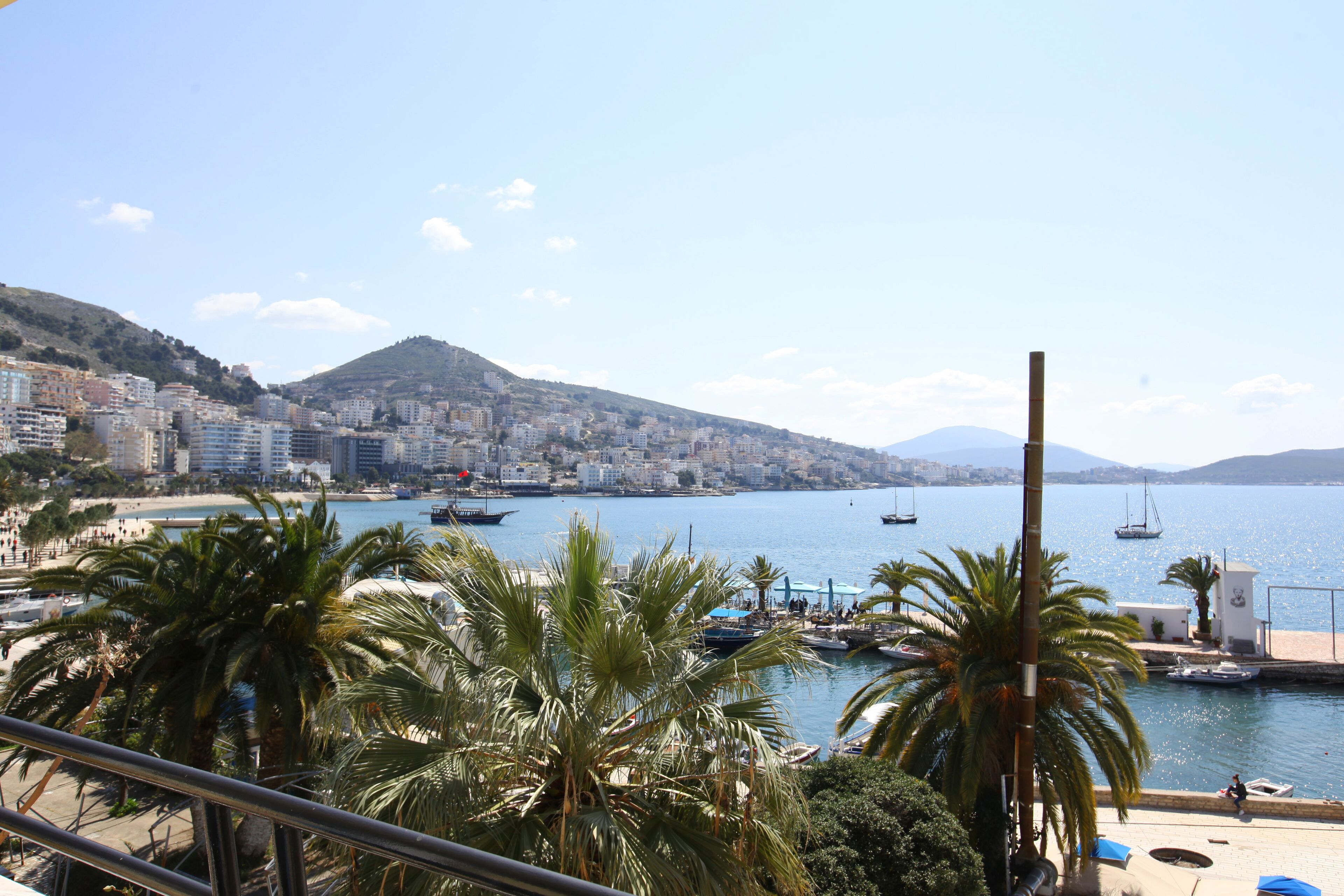 A coastal cityscape with a marina, palm trees, and buildings along the waterfront.