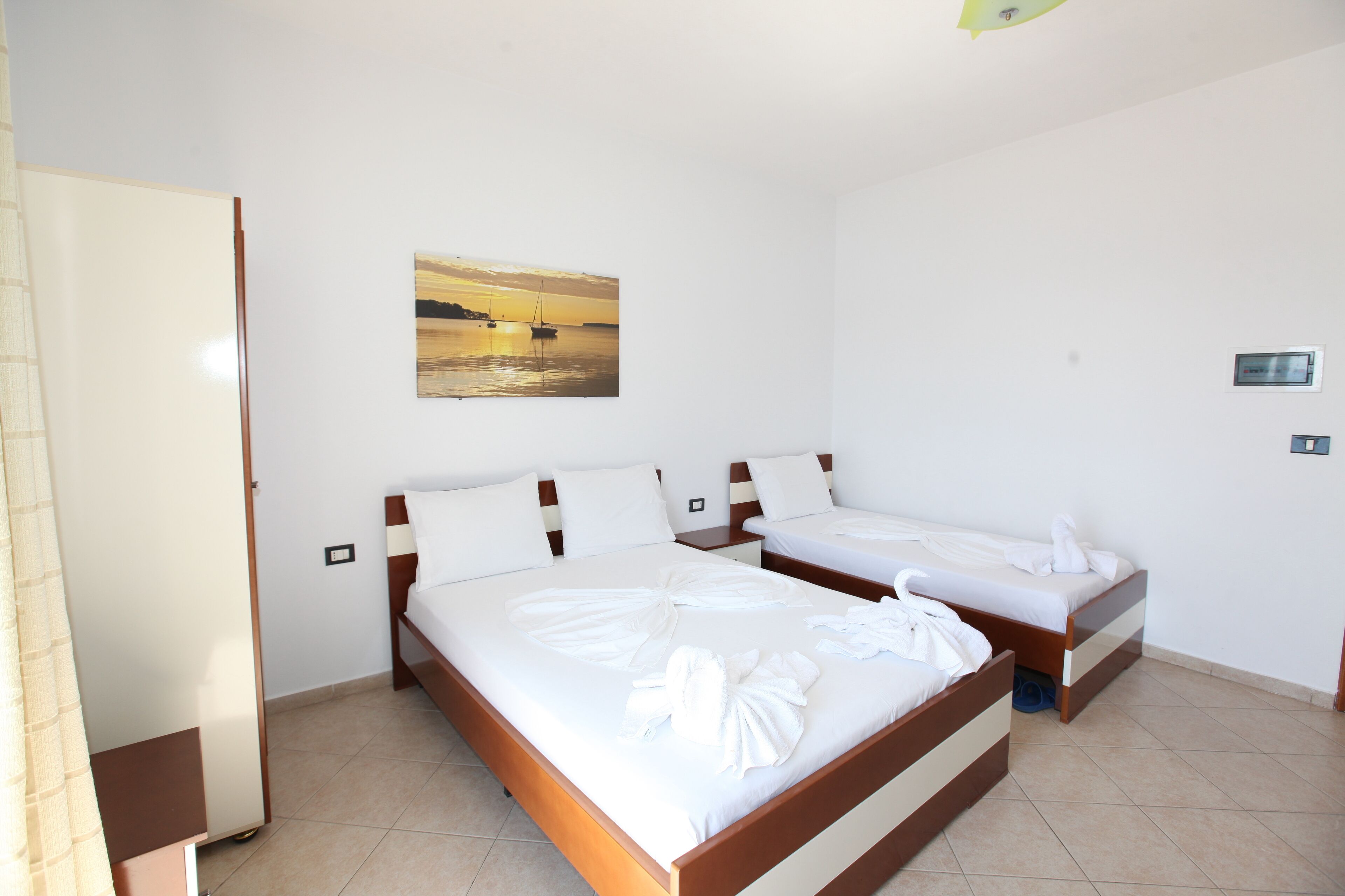 A hotel room with two beds, a painting on the wall, and a door.