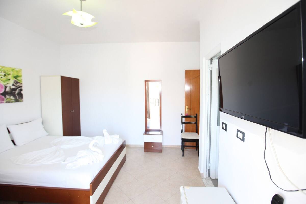 A hotel room with a bed, a TV, a wardrobe, and a mirror.