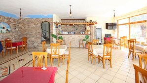 A spacious dining area with wooden tables and chairs, a brick wall, and a bar area with shelves and potted plants. - Hotel Real (Sarandë)