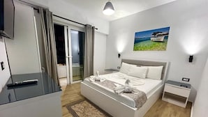A modern hotel room with a large bed, a flat-screen TV, a bedside table, and a view of the sea through the window. - Hotel Real (Sarandë)