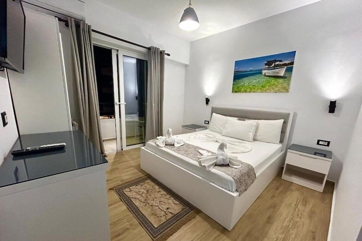 A modern hotel room with a bed, a desk, a chair, a TV, and a painting on the wall.