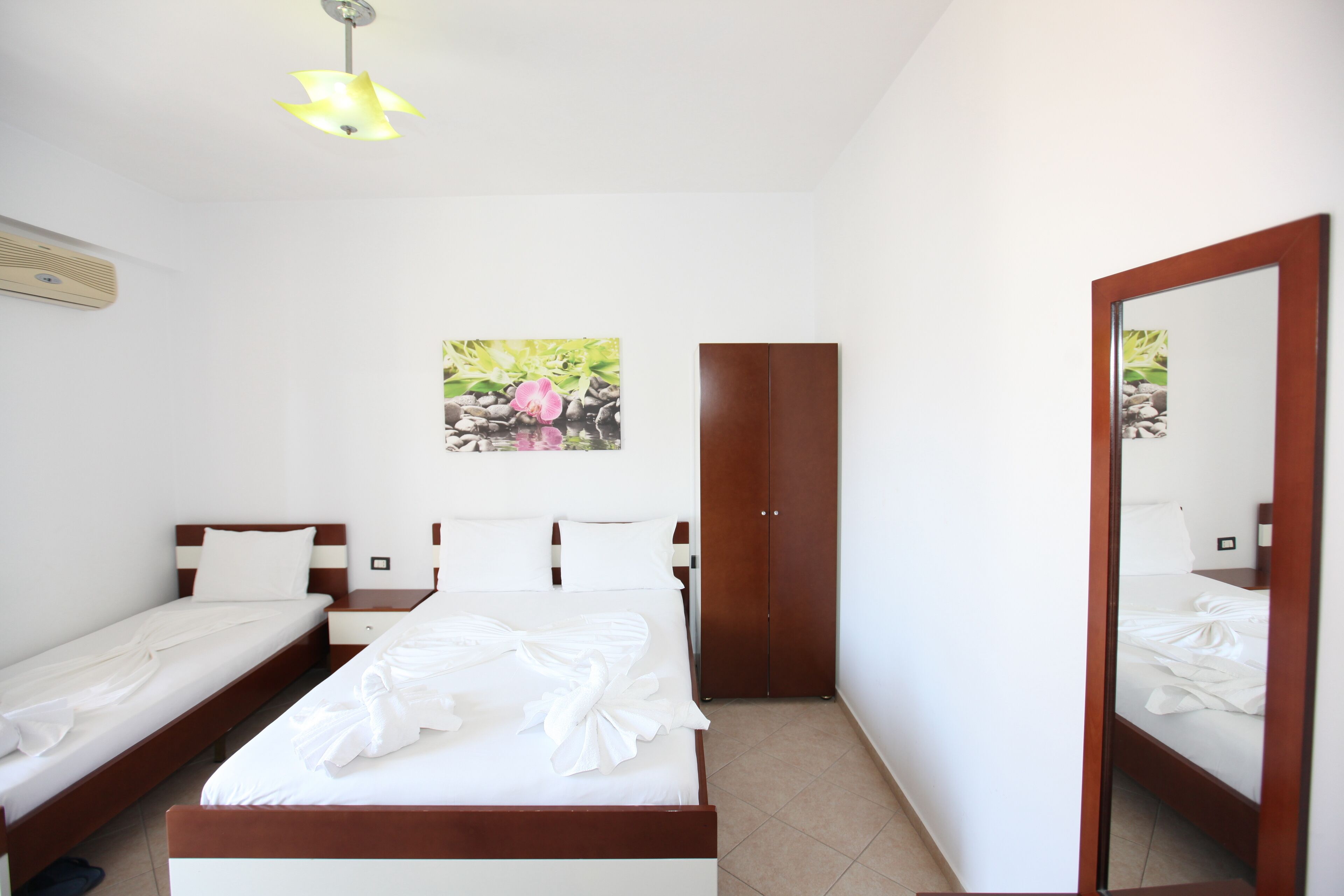 Une chambre d’hôtel comprenant un lit, deux tables de chevet, une armoire, un miroir et un luminaire au plafond.