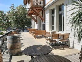 An outdoor seating area with wooden tables and benches, a decorative wooden balustrade, and a large window.