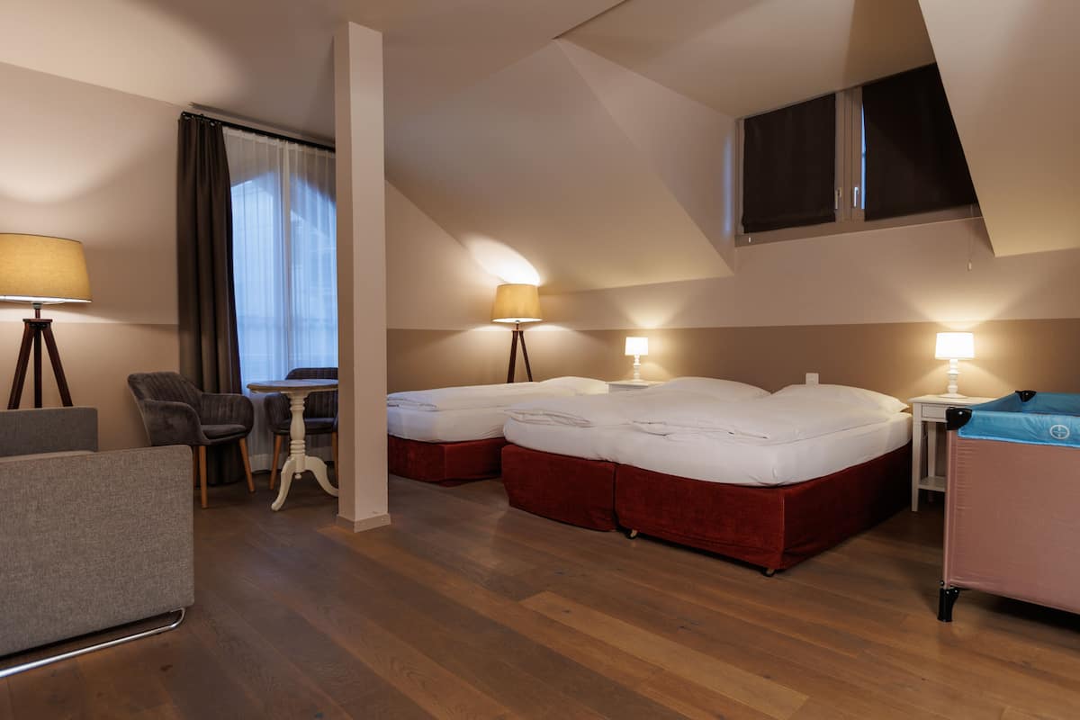 A hotel room with two beds, a desk, a chair, and a lamp.