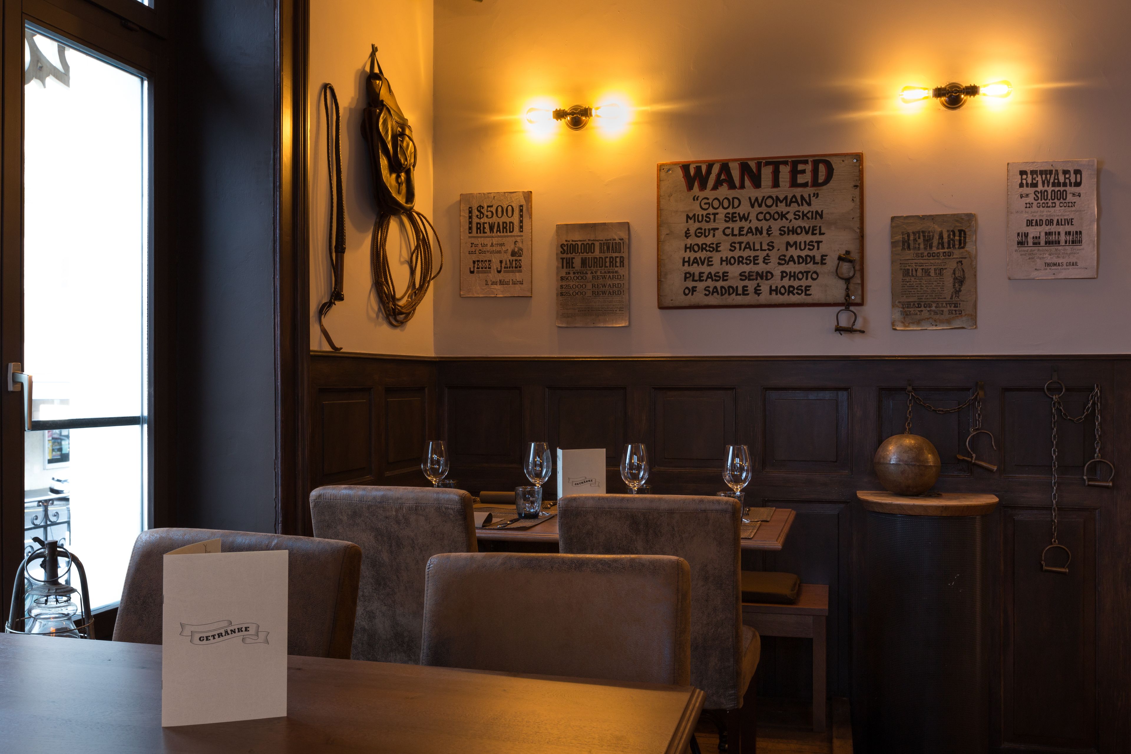 A restaurant interior with wooden paneling, a menu stand, and vintage wanted posters on the wall.