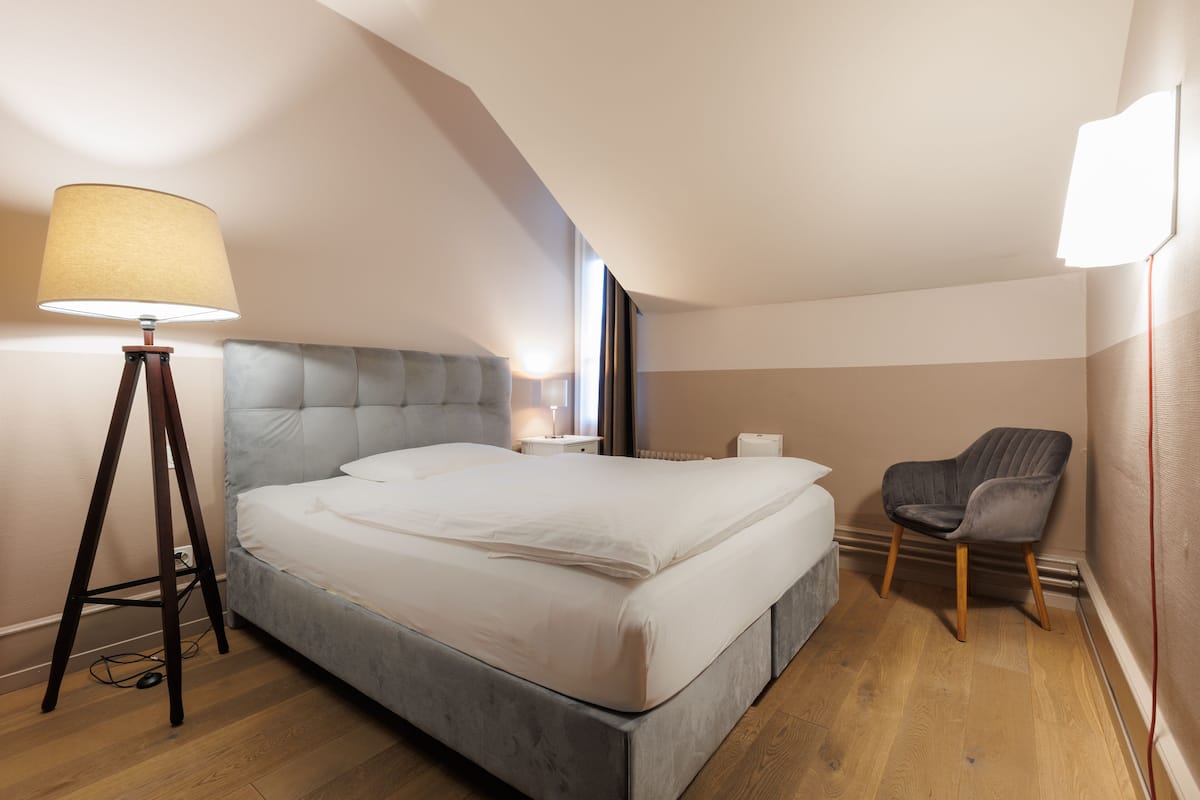 A modern bedroom with a large bed, a bedside lamp, a chair, and a window.