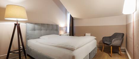 Un dormitorio moderno con una cama grande, una lámpara de noche, una silla y una ventana.