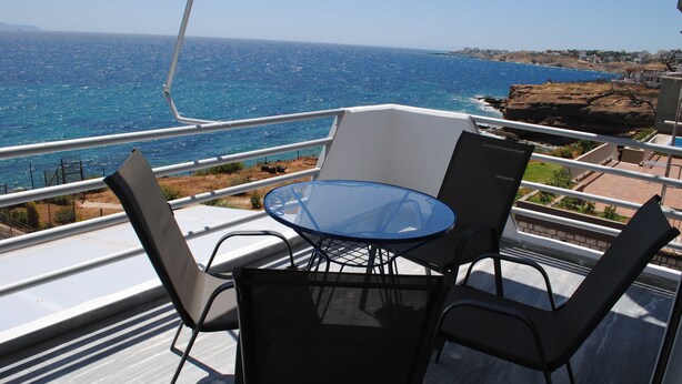 En balkon med et glasbord og stole, der giver udsigt over kysten.