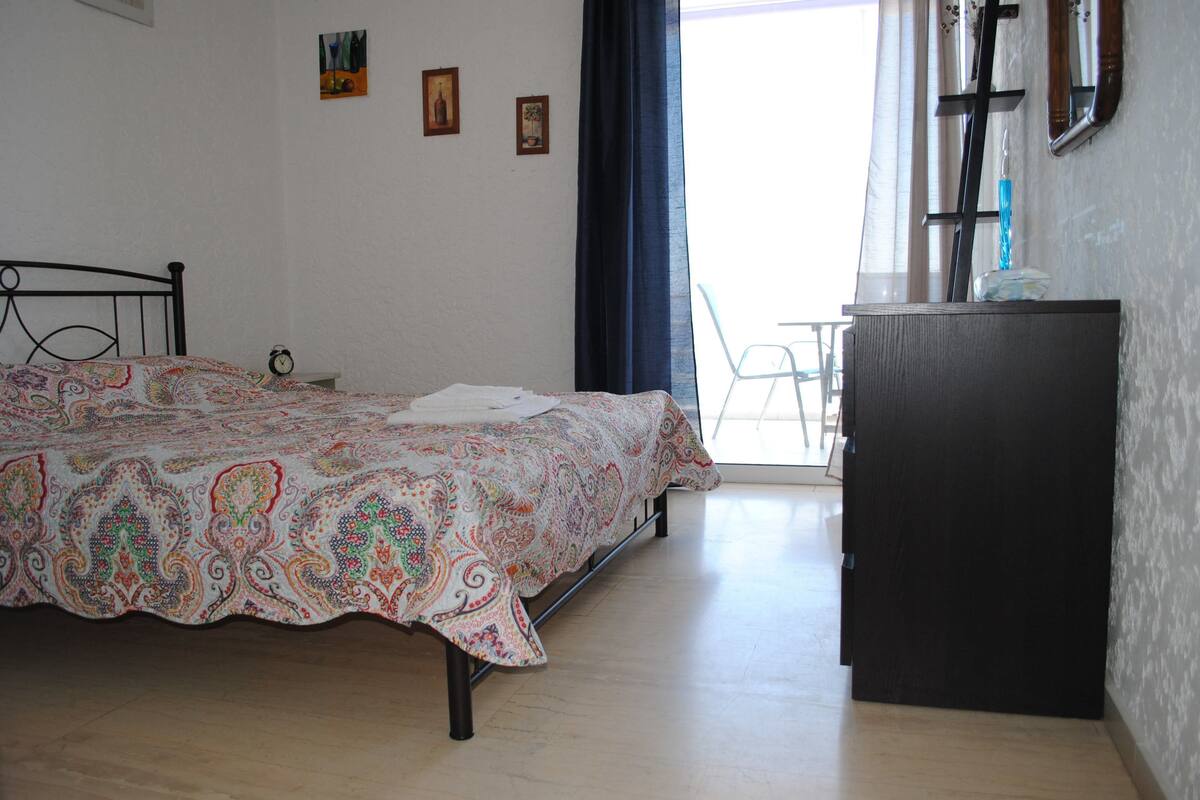 Une chambre à coucher avec un lit, une commode, une chaise et une fenêtre avec des rideaux.