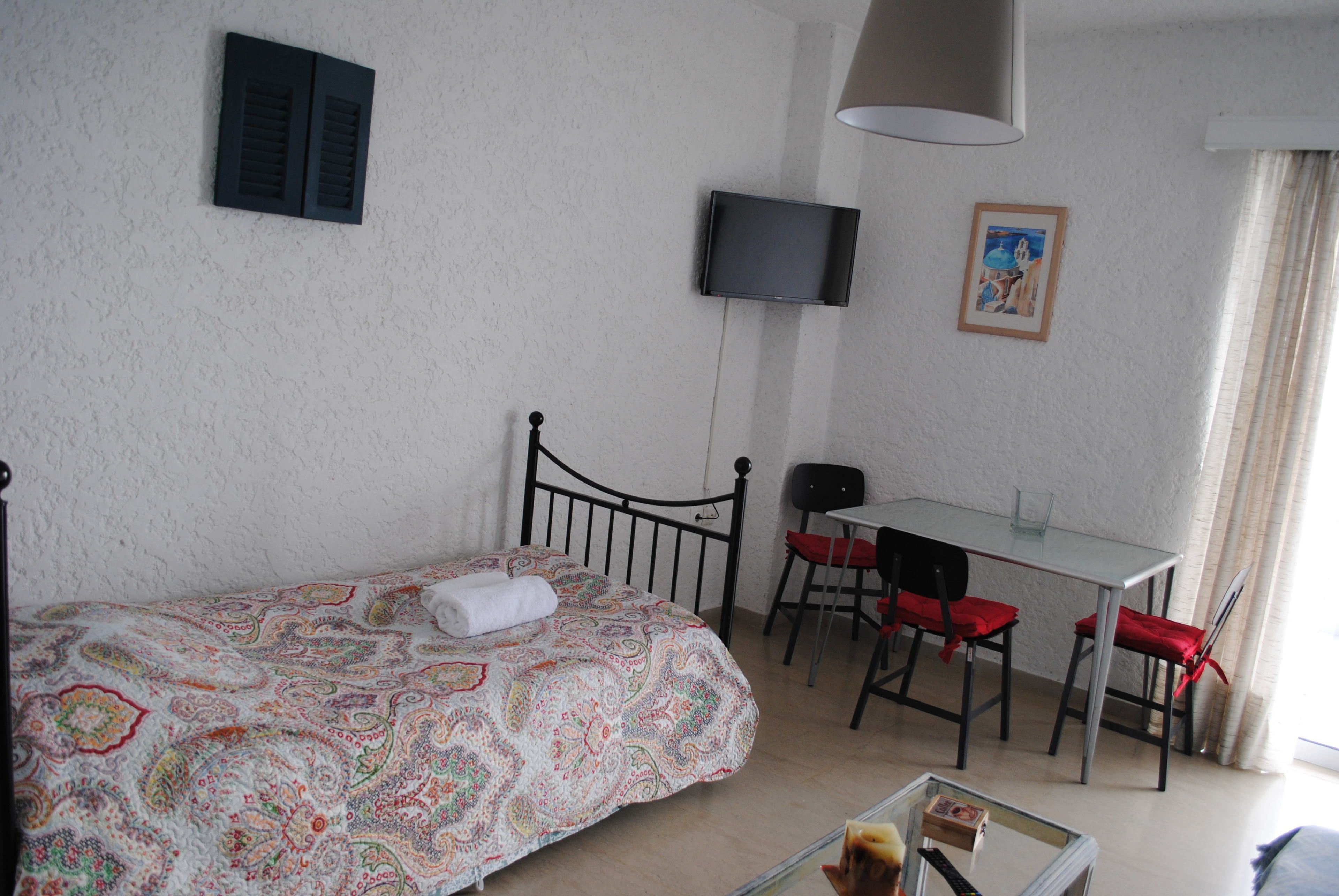 Una camera da letto con un letto, una scrivania, due sedie, una televisione e un quadro appeso al muro.