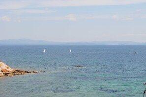 A coastal view with calm waters, a rocky shoreline, and distant mountains. - Andromachi Apartments (Rafina-Pikermi)