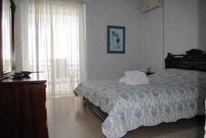A bedroom with a bed, a dresser, a framed picture on the wall, and a window with sheer curtains. - Andromachi Apartments (Rafina-Pikermi)