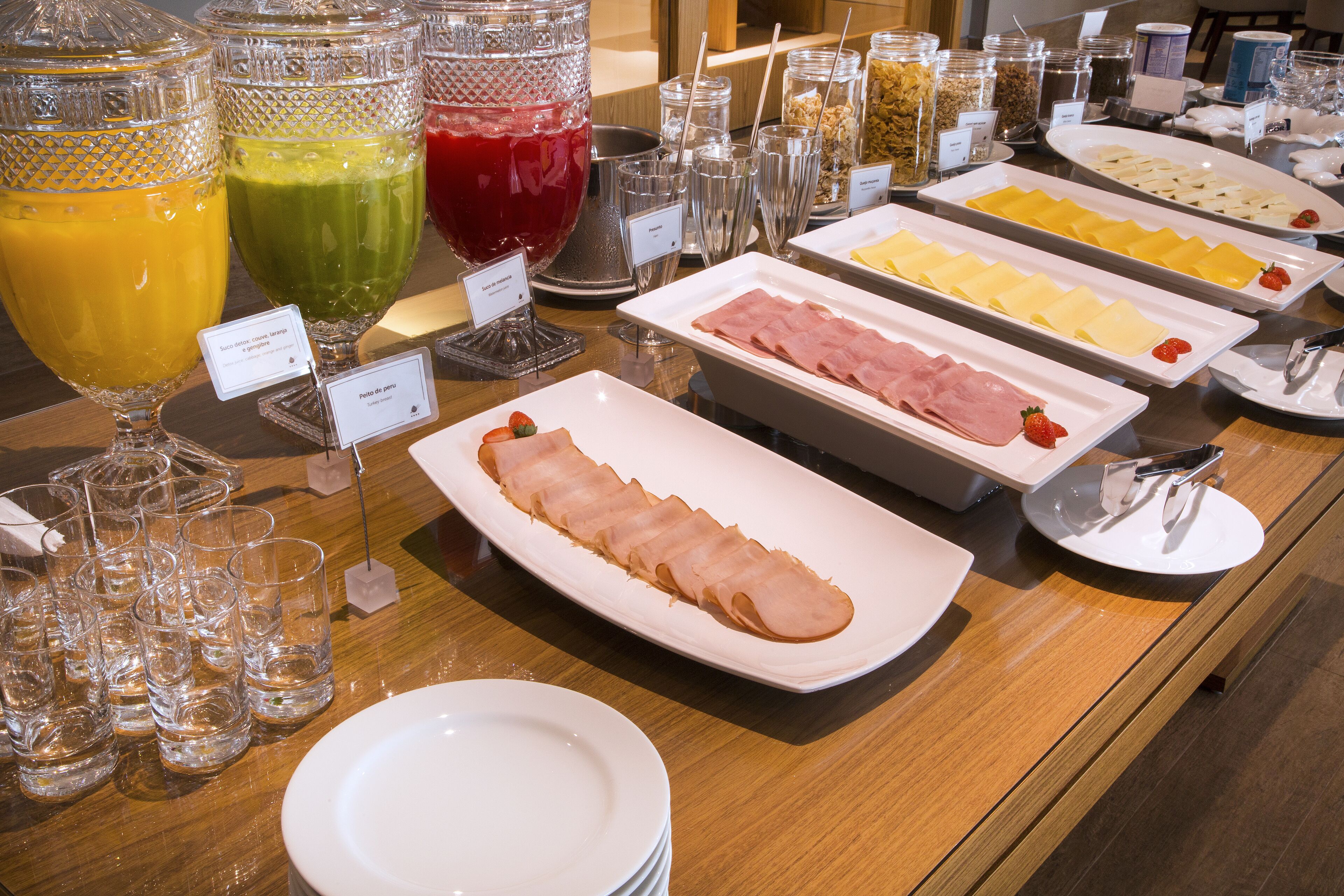 Un bufé con diversas opciones de comida, incluyendo embutidos, quesos y jugos de frutas.