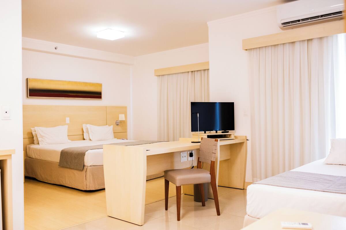Une chambre d’hôtel comprenant un lit, un bureau avec une chaise, une télévision et une fenêtre avec des rideaux.