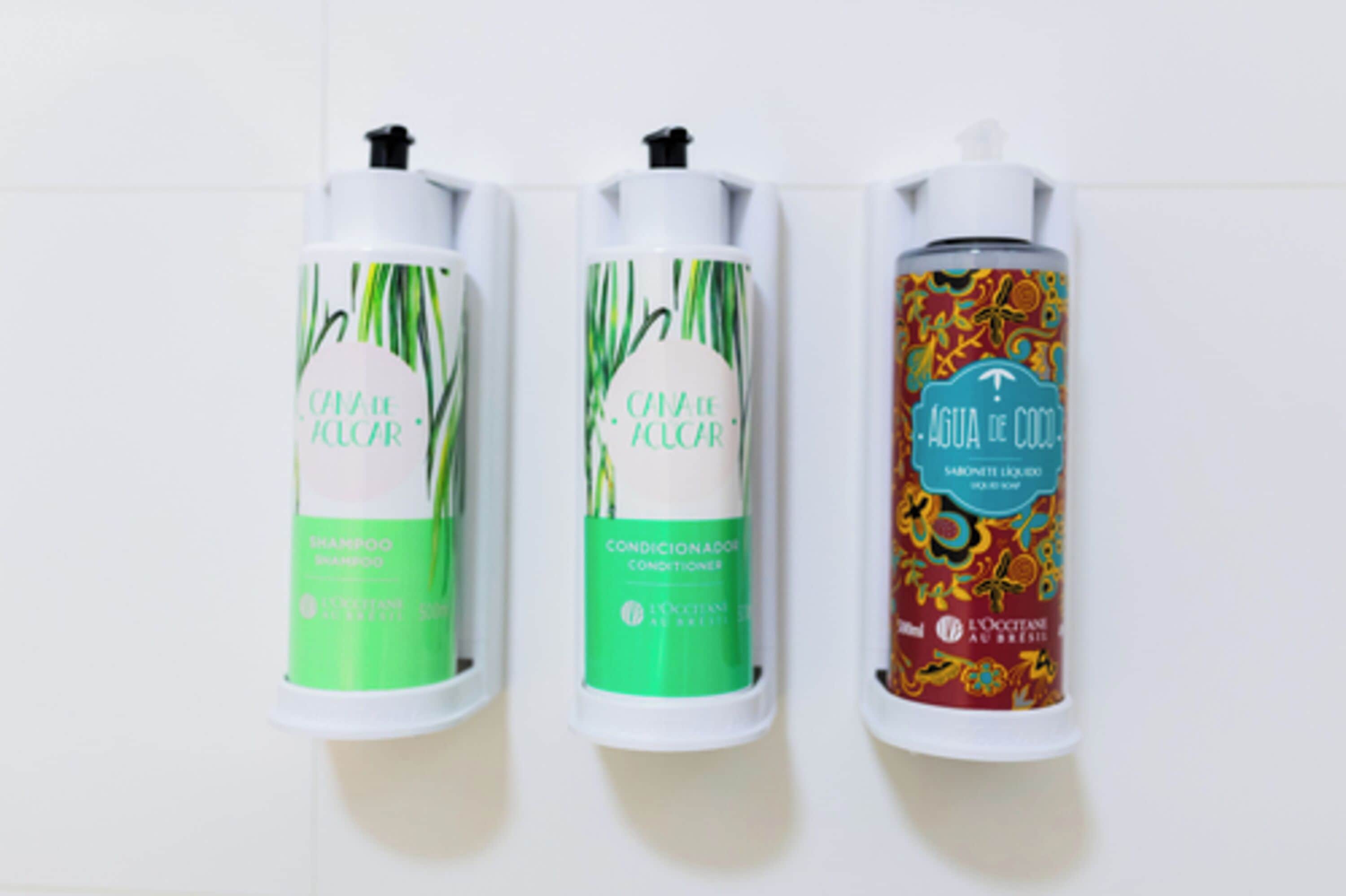 Três frascos de shampoo, condicionador e sabonete dispostos sobre uma superfície branca.