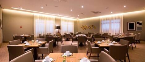 Ein Hotelrestaurant mit mehreren Tischen und Stühlen, ansprechend auf einem großzügigen Grundriss angeordnet.