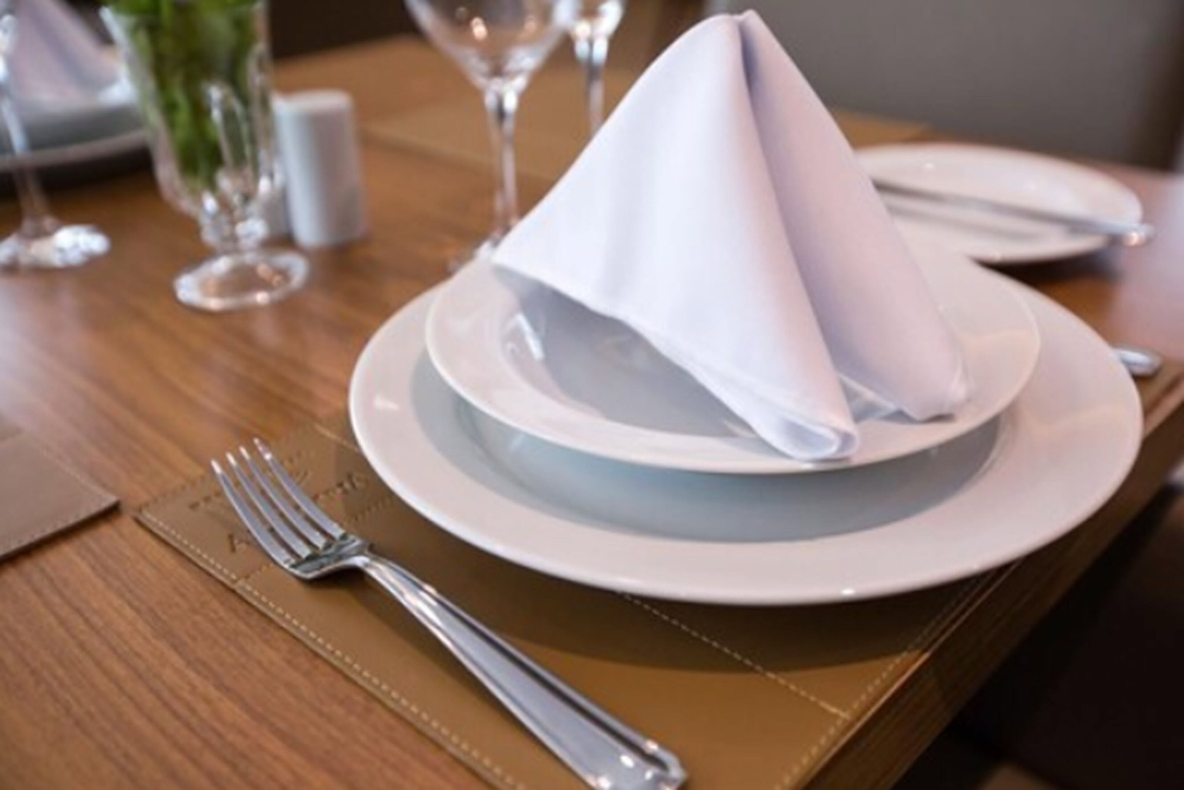 A neatly set dining table with a folded napkin, a fork, and a glass of water.