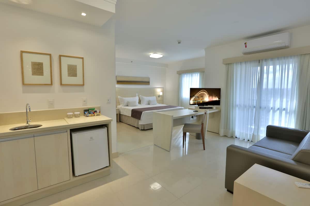 Une chambre d’hôtel équipée d’un lit, d’un bureau, d’une télévision, d’un canapé et d’une kitchenette.