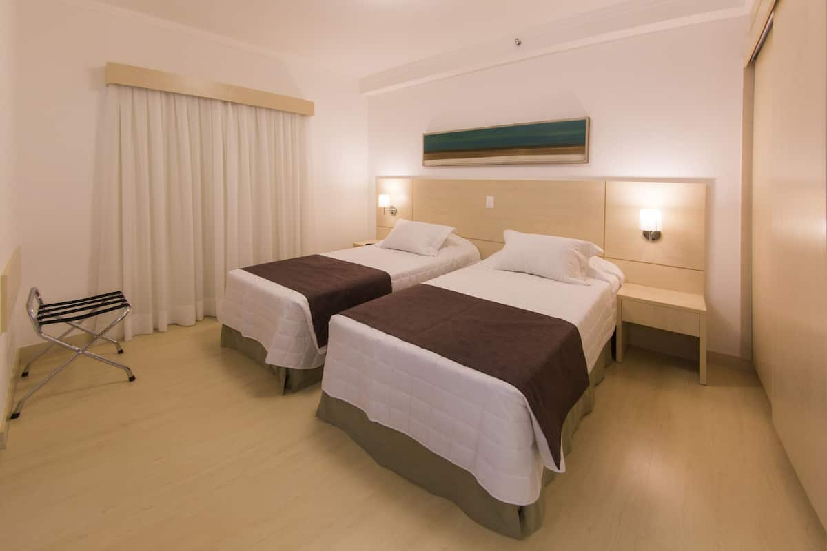 Une chambre d’hôtel avec deux lits, une petite table, une chaise et un tableau au mur.