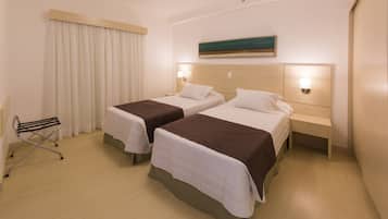 A hotel room with two beds, a small table, a chair, and a painting on the wall.