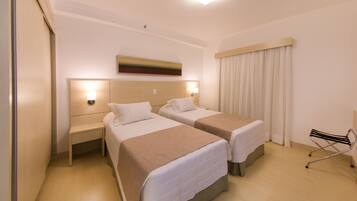Quarto de hotel com duas camas, uma mesinha de cabeceira, uma cadeira e um quadro na parede.