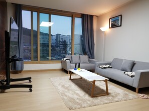 Una sala de estar moderna con un sofá gris, una mesa de centro blanca y un televisor sobre un mueble.