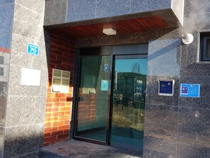 Ein Gebäudeeingang mit Glastür, Backsteinwand und einem blauen Schild, das einen Parkplatz kennzeichnet.
