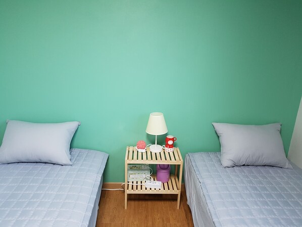 Una habitación con dos camas, una mesita de noche con lámpara y un pequeño estante con objetos decorativos.