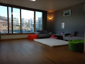 Ein modernes Wohnzimmer mit großem Fenster, einem grauen Sofa, einem roten Sitzsack und einem grünen Sitzsack sowie einem weißen Teppich.