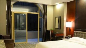 A hotel room with a large bed, a desk, a chair, a TV, and a sliding glass door leading to a balcony. - Enping Jinzhou Holiday Hotel (Jiangmen)
