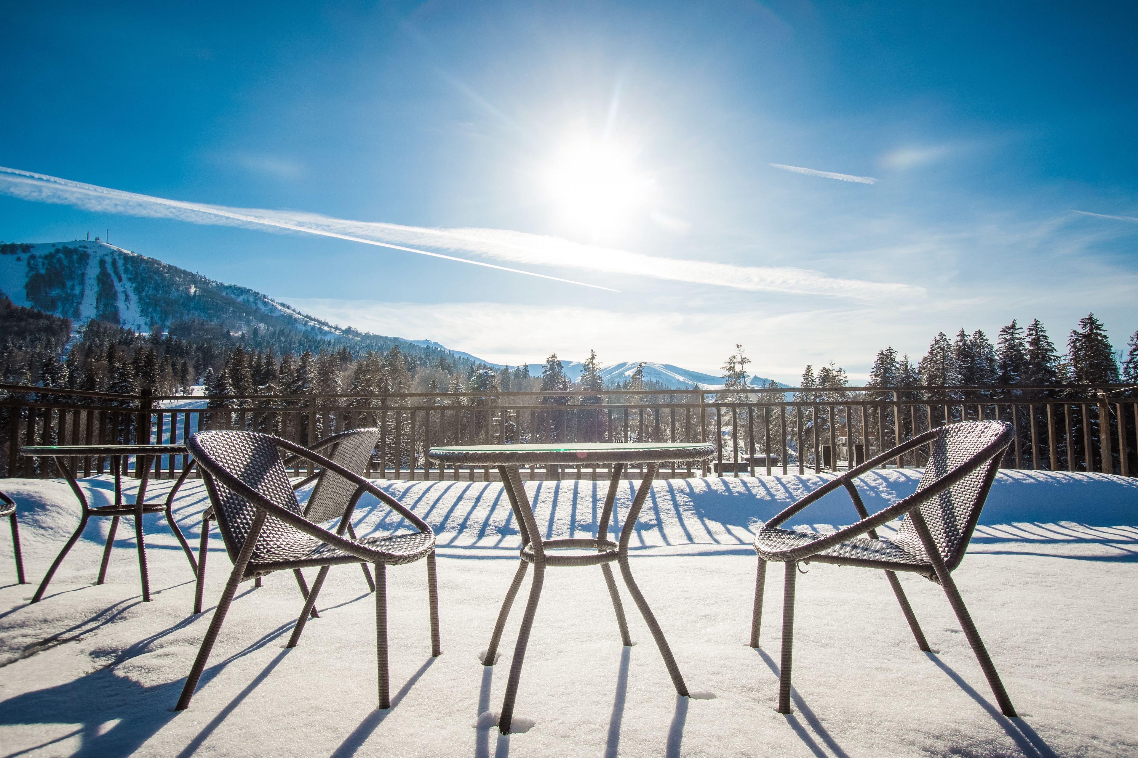 A snow-covered outdoor seating area with metal chairs and a table, overlooking a mountainous landscape.